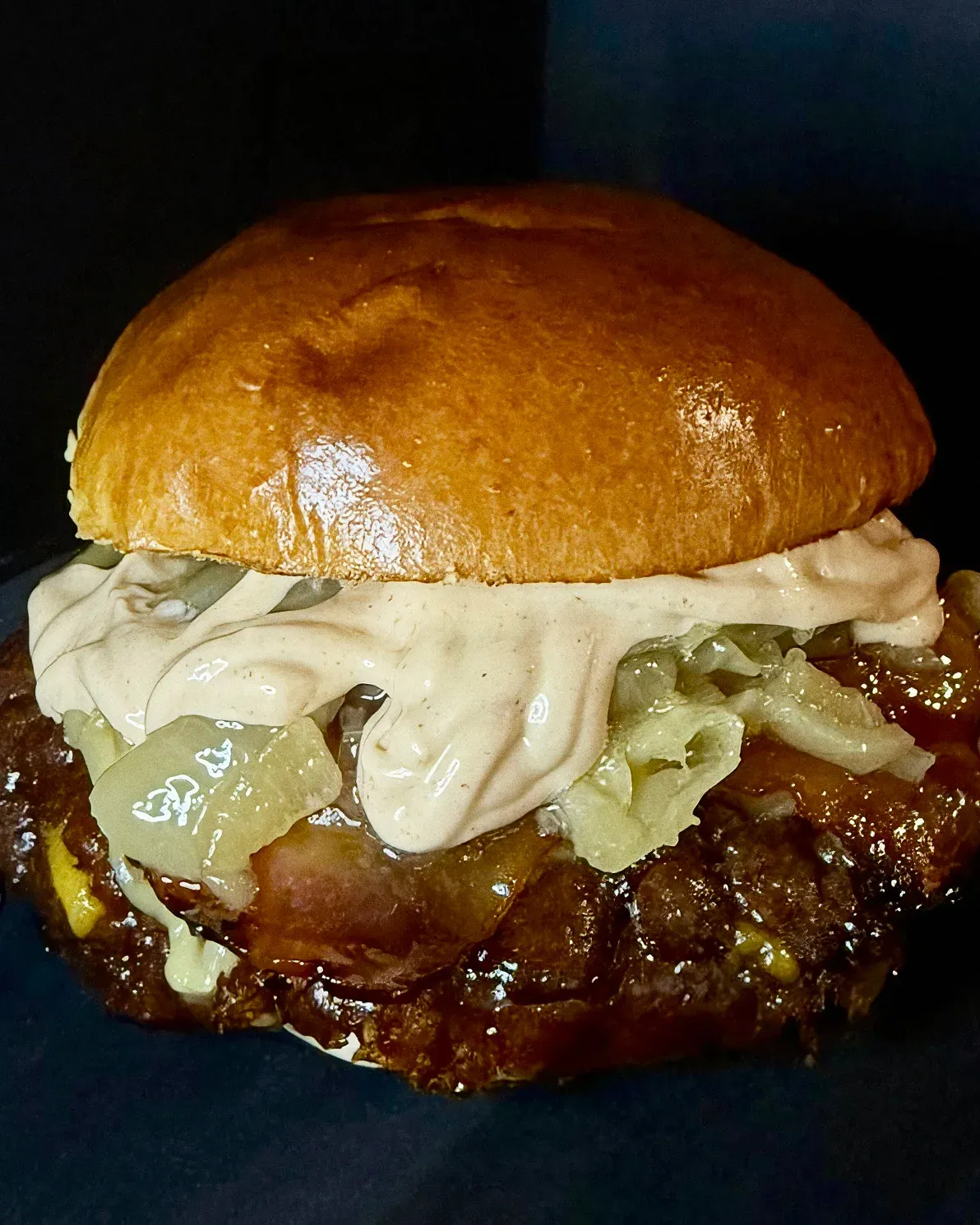 Smash burger con cebolla pochada y salsa cremosa sobre fondo oscuro